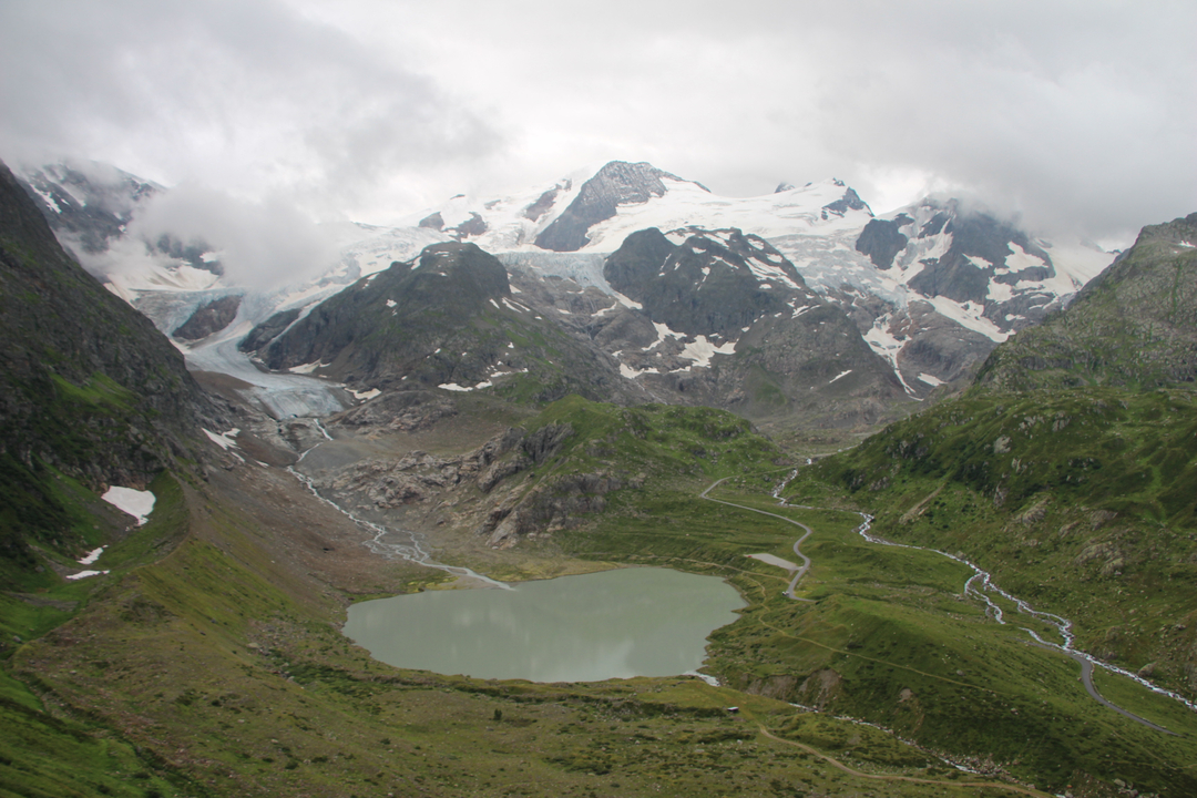 Mountain landscape with a lake, snow, and winding paths.