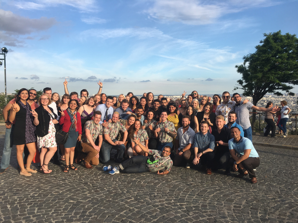 Un grand groupe de personnes souriant et posant avec une vue pittoresque de la ville en arrière-plan.