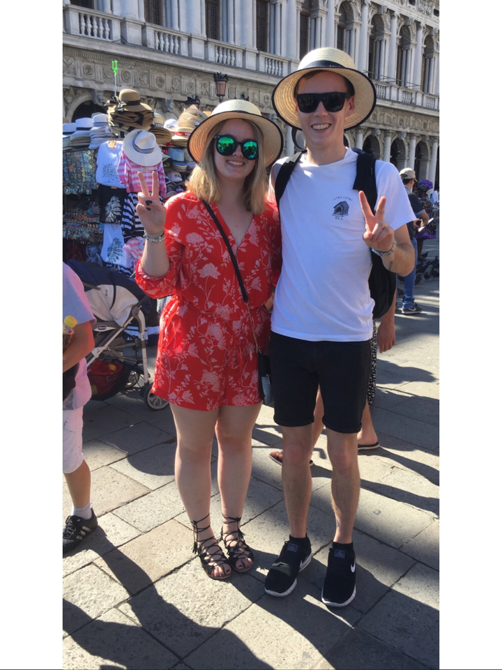 Deux personnes se tenant ensemble dans un lieu extérieur, l'une en robe rouge et l'autre en chemise blanche.