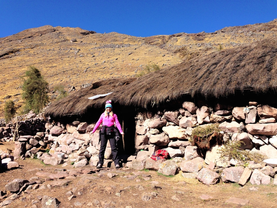Randonneur aux vêtements colorés devant une cabane en pierre.