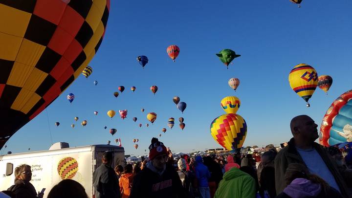 Une foule regardant des montgolfières décoller dans un ciel bleu dégagé.