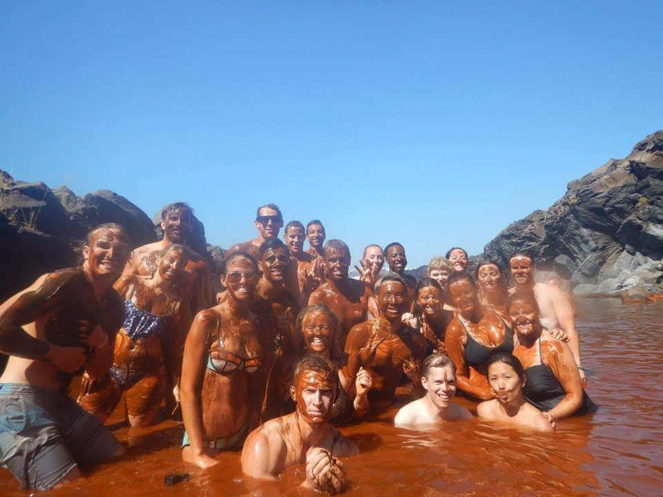Group of people covered in mud posing in water.