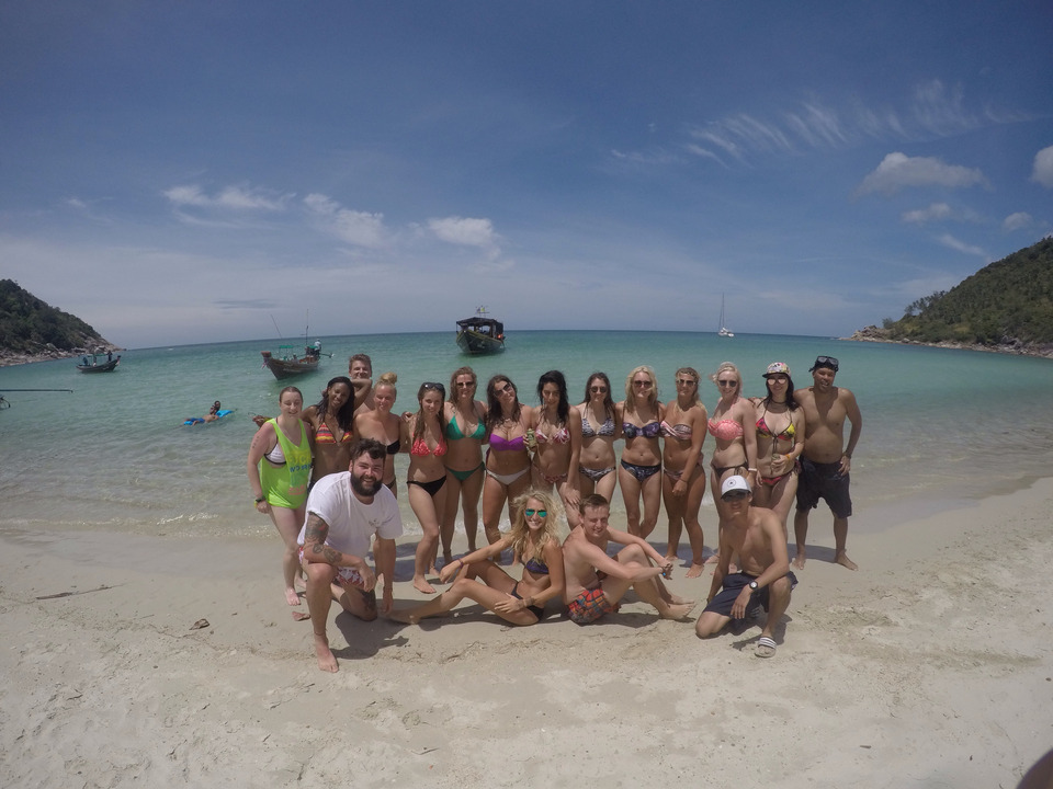Group photo of people on a beach with boats and blue water.