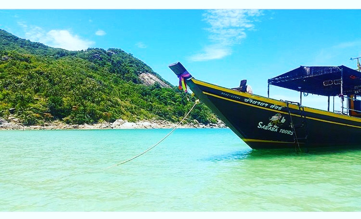 A boat in clear turquoise water with lush green hills in the background.