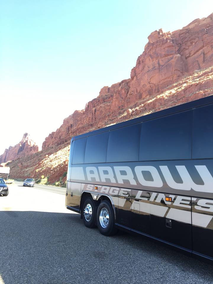 Bus touristique garé près de formations rocheuses rouges par une journée ensoleillée.