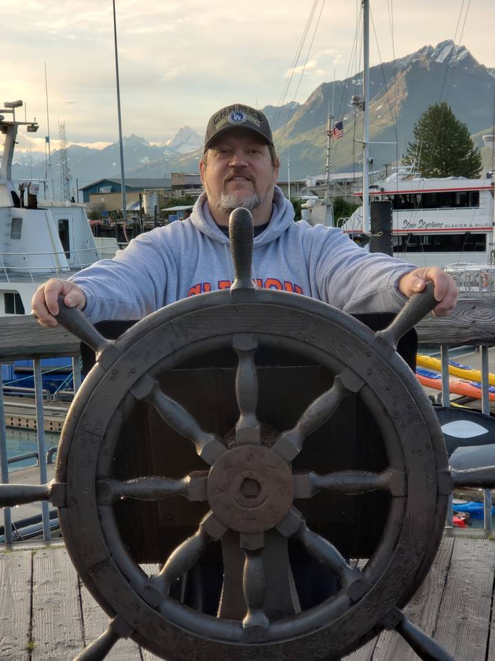 Personne tenant un gouvernail de navire avec des montagnes en arrière-plan.