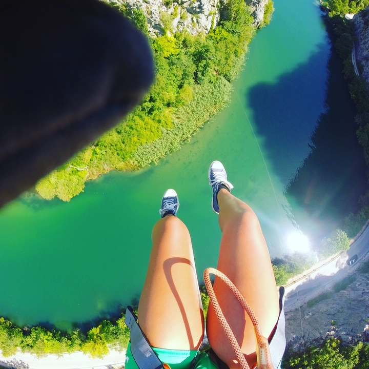 Feet dangling above green water and vegetation.
