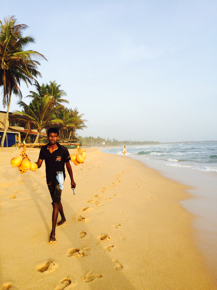 Homme tenant des noix de coco marchant sur une plage avec des vagues.