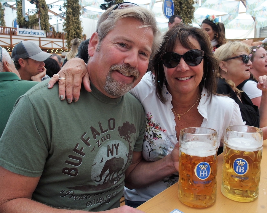 Couple souriant avec de grandes chopes de bière lors d'un festival en plein air.