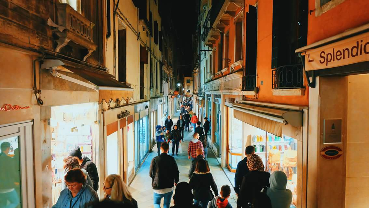 Busy narrow street with people shopping at night.