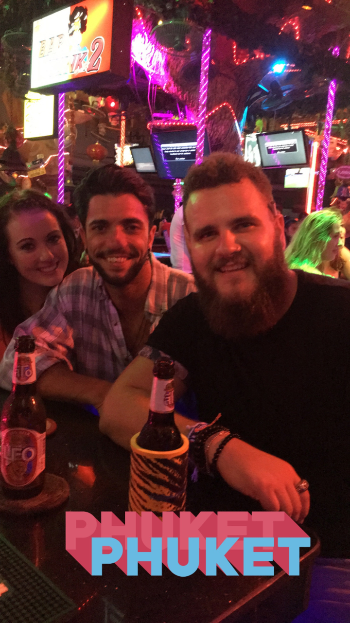 Three friends sitting at a bar holding drinks.