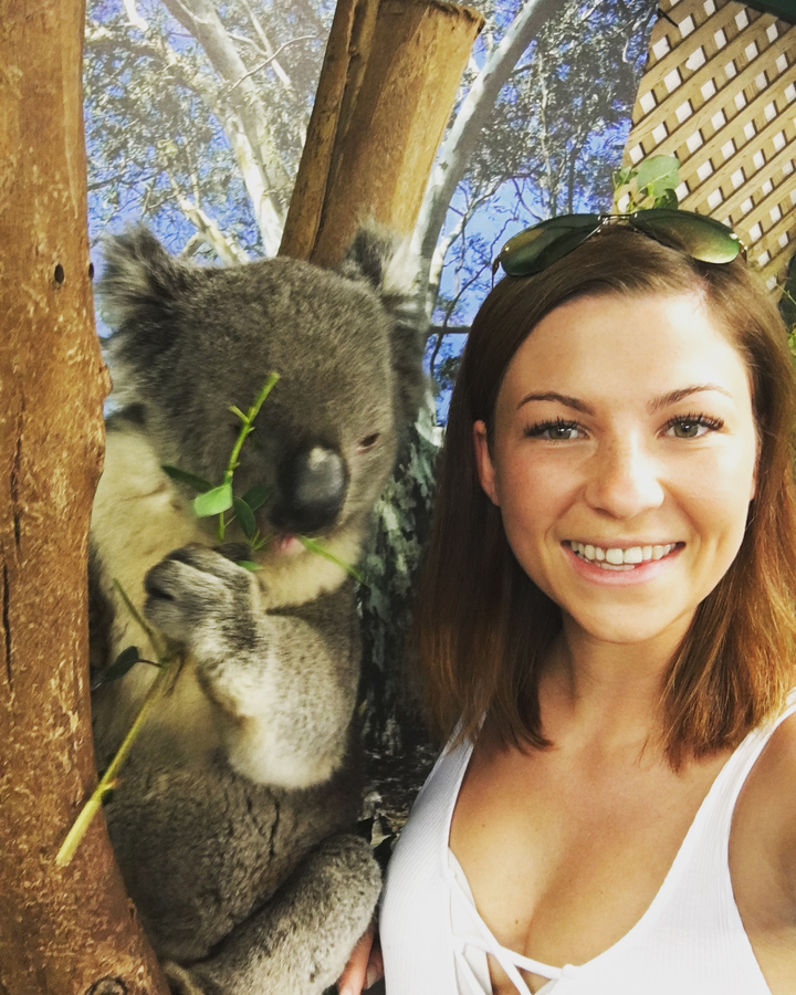 A person smiling with a koala eating leaves.