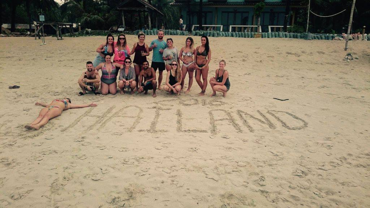 Group on a beach with the word 'THAILAND' written in sand.