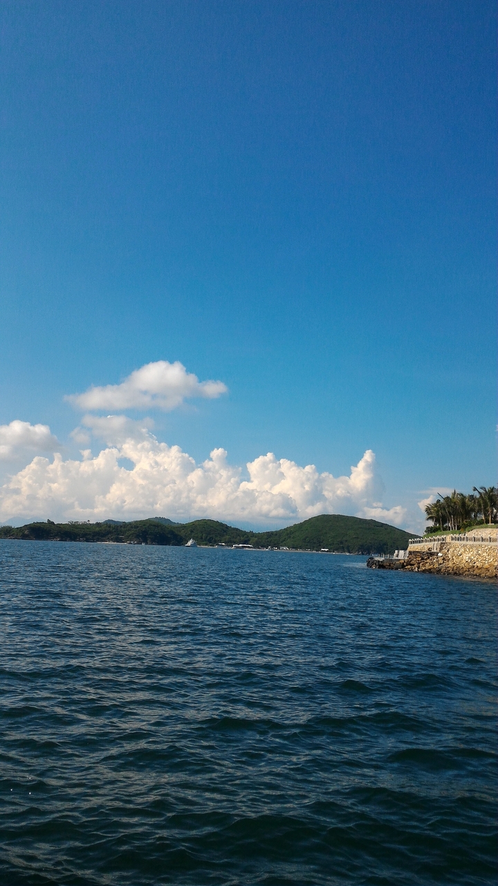 Mer calme avec des collines lointaines sous un ciel bleu.