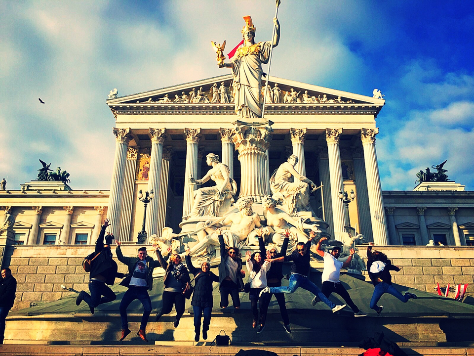 Des personnes sautent devant un grand bâtiment néoclassique.