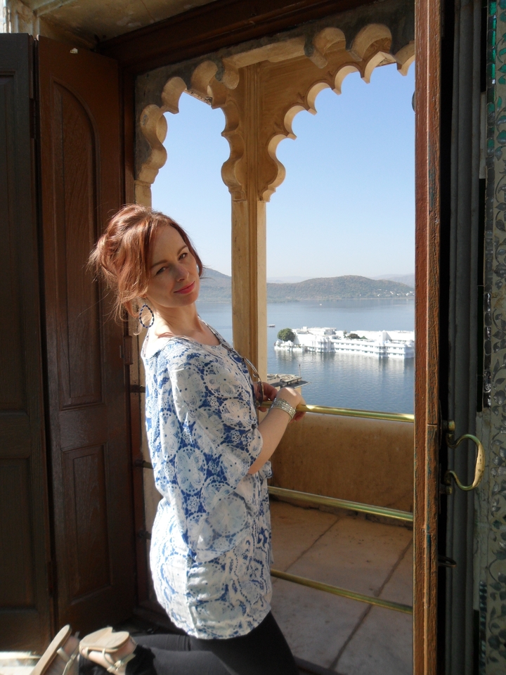 Traveler smiles from a palace window overlooking Lake Palace in Udaipur.