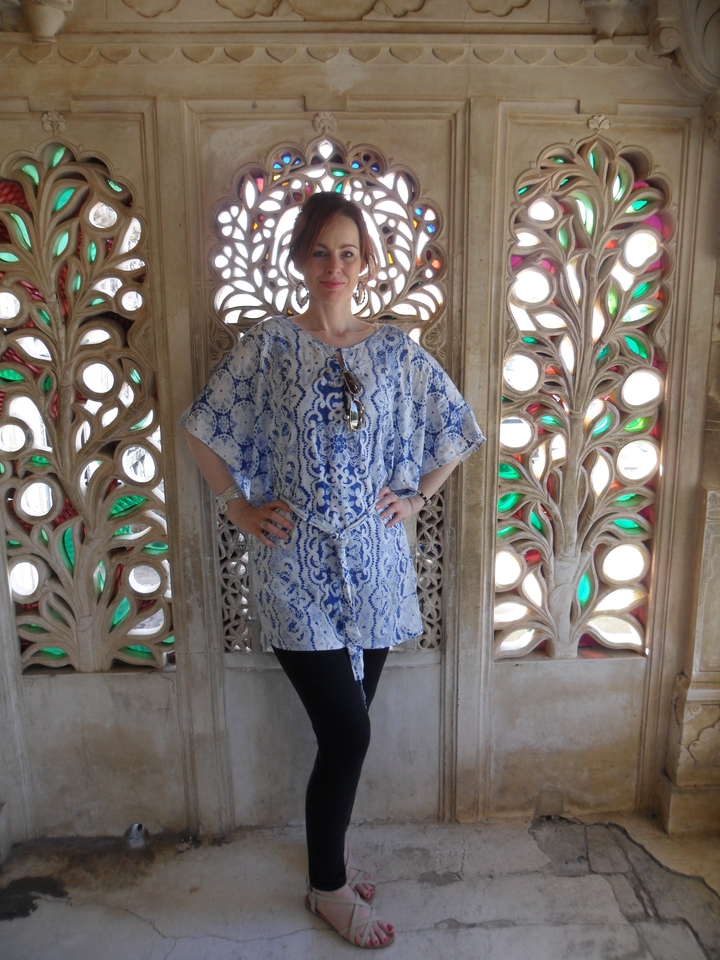 Woman poses against an intricately carved stone lattice with colored glass inlays.
