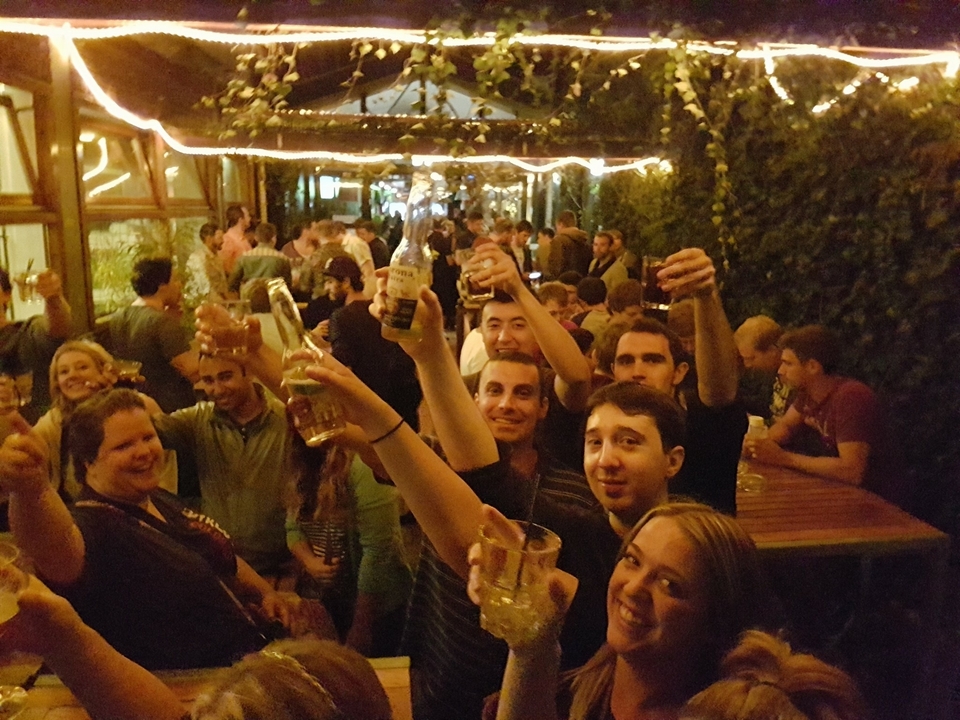 Des personnes dans un bar, en plein air, brandissant des boissons.