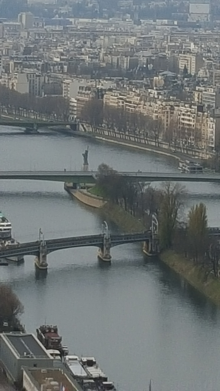 Vue à distance d'une rivière avec un pont et une petite statue.