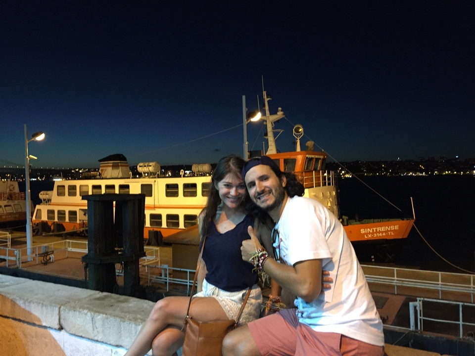 Deux personnes posant devant un grand ferry pendant la nuit.