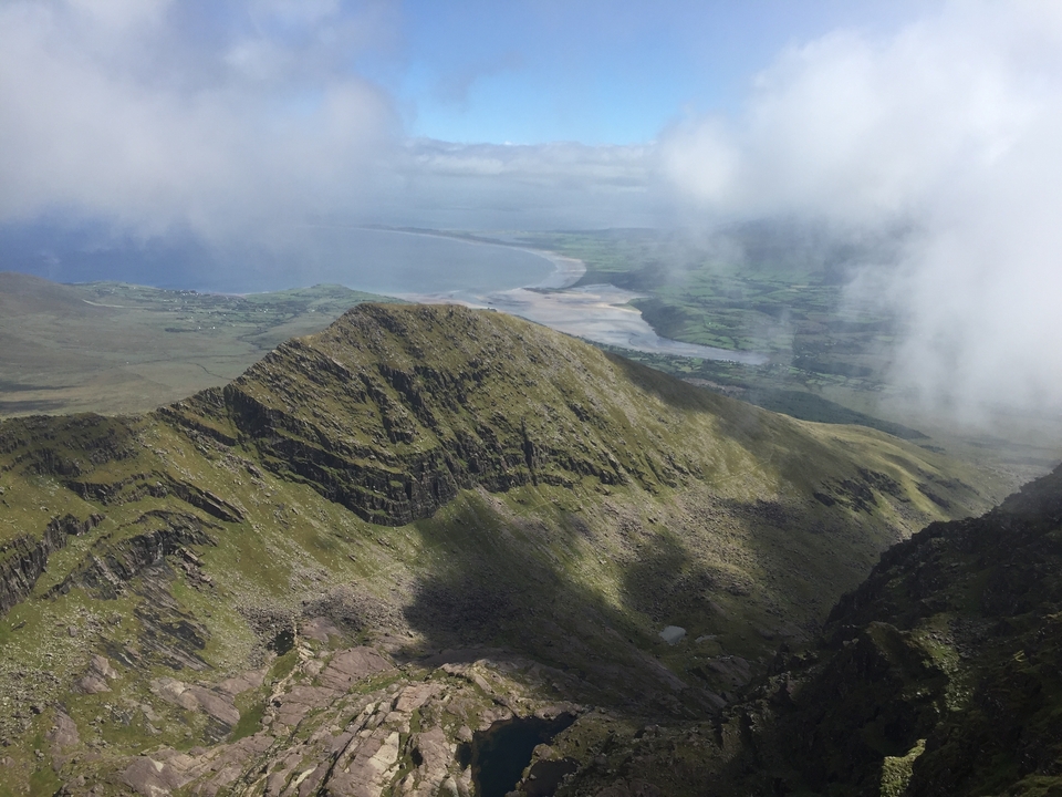 Paysage de montagne avec ciel nuageux et mer au loin.