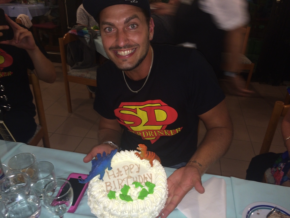 Personne tenant un gâteau d'anniversaire décoré, souriant à l'appareil photo.