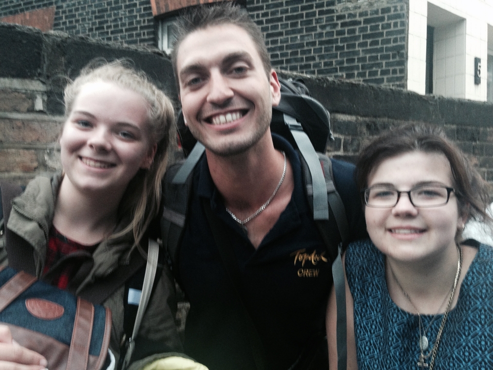 Trois personnes posant devant un mur de pierre avec des sacs à dos.