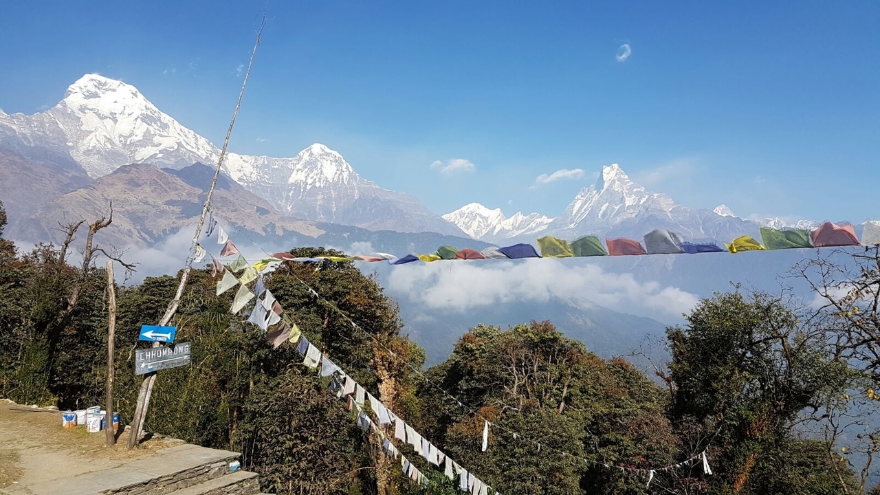 Vue de la montagne avec des drapeaux de prière et des sommets enneigés.