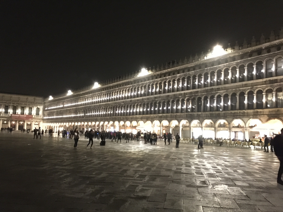 Brightly lit historic square with people walking.