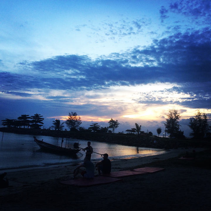 People and a boat with a sunset over the water.