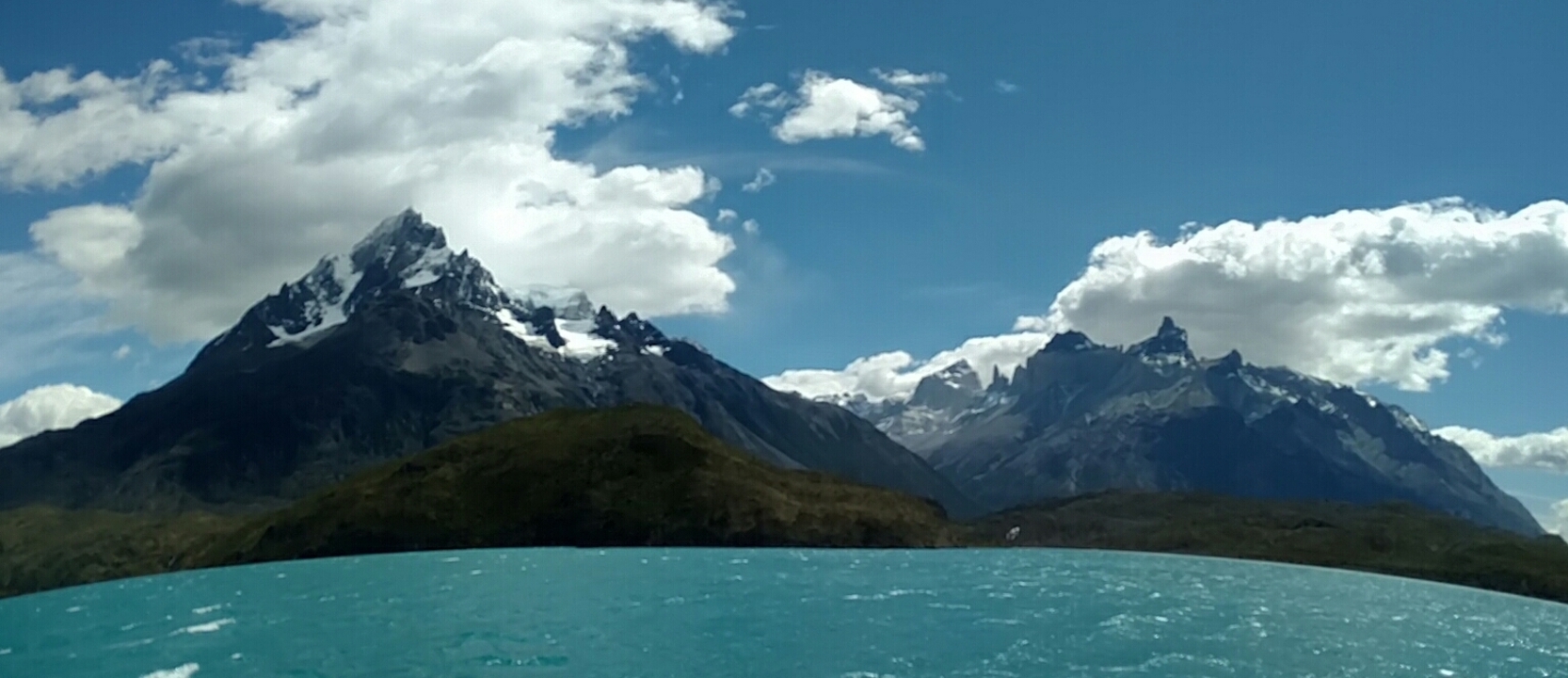 Chaîne de montagnes avec ciel nuageux et eau bleue.