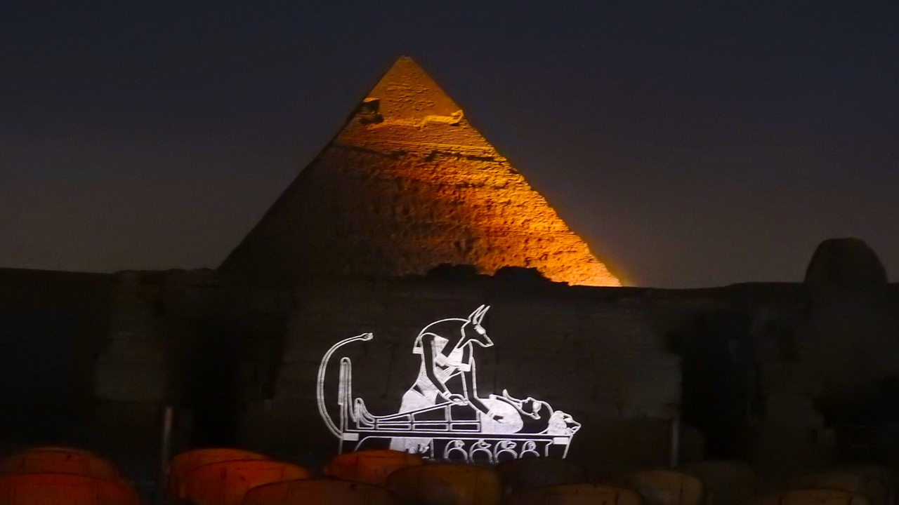 Pyramid illuminated at night with Egyptian symbols.