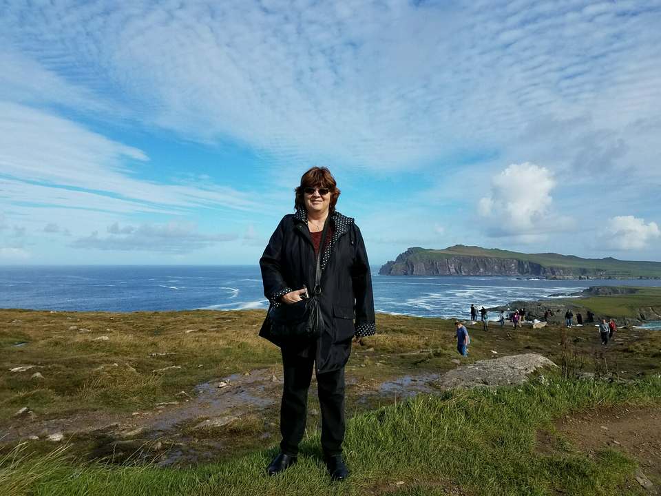 A person posing on a scenic coastal cliff.