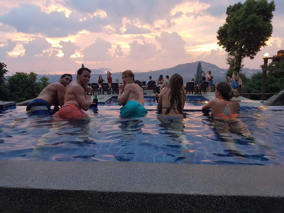 Group of people relaxing in a pool with a sunset view.