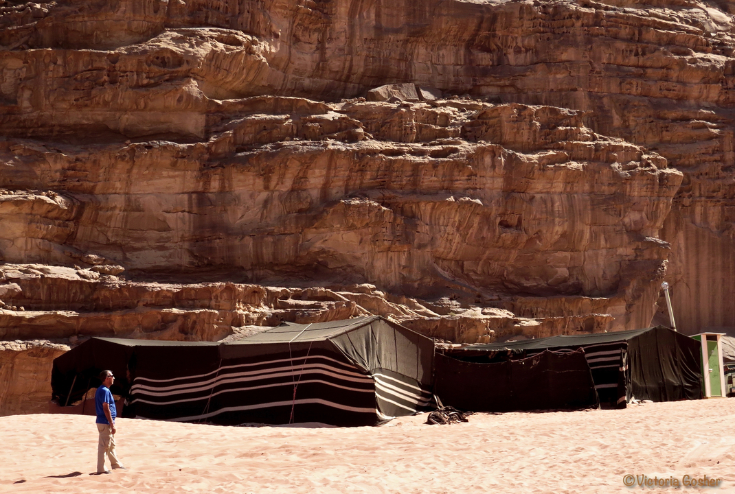 Homme marchant devant des tentes sur fond rocheux.