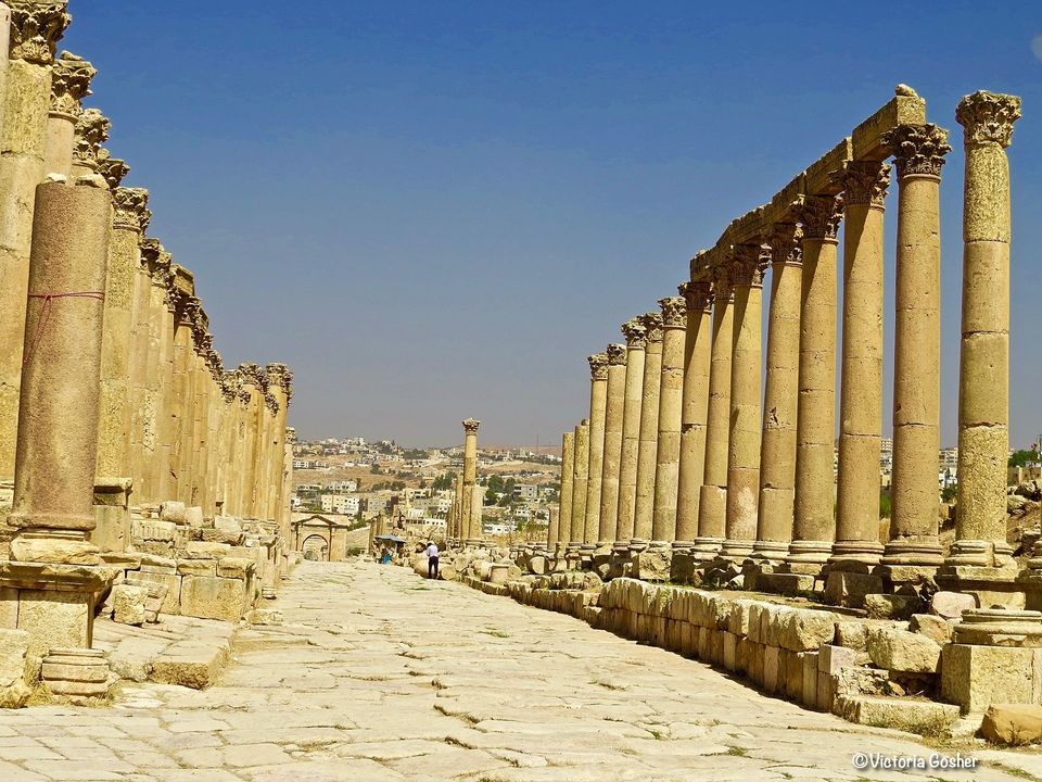 Ancienne rue à colonnades avec paysage urbain en arrière-plan.