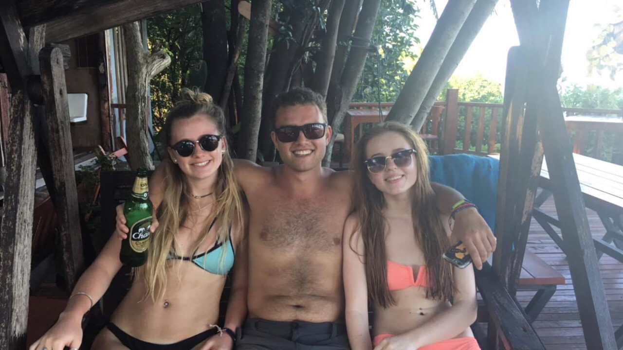Three people sitting on a bench with one holding a beer bottle.
