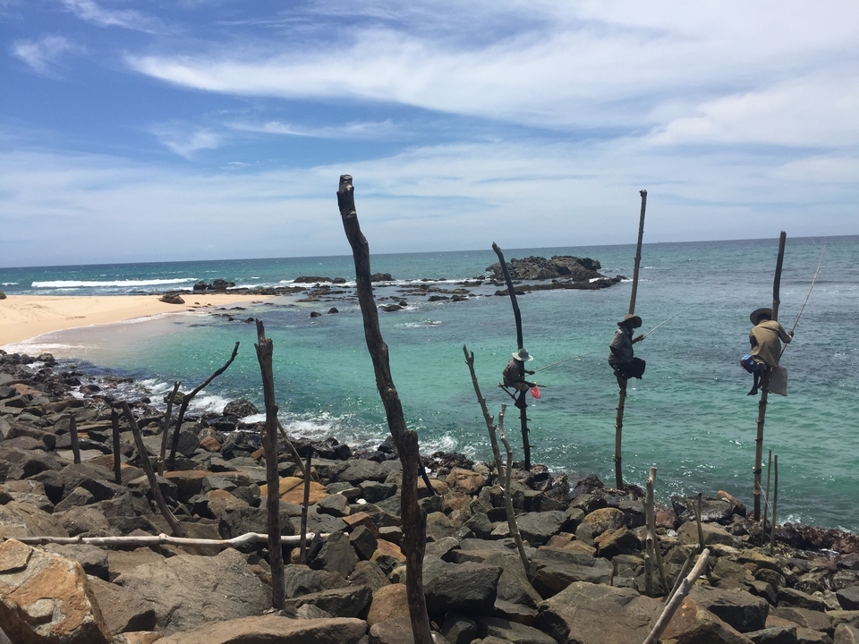 Des personnes pratiquant la pêche traditionnelle sur pilotis dans un magnifique paysage marin.
