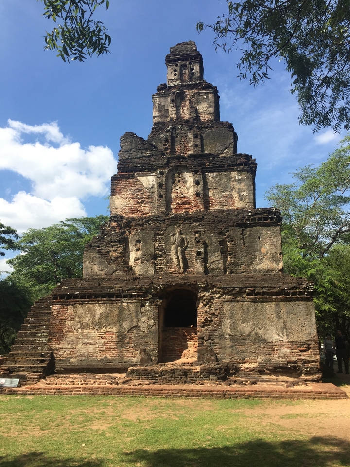Ancienne tour en briques avec des sculptures entourée de verdure.