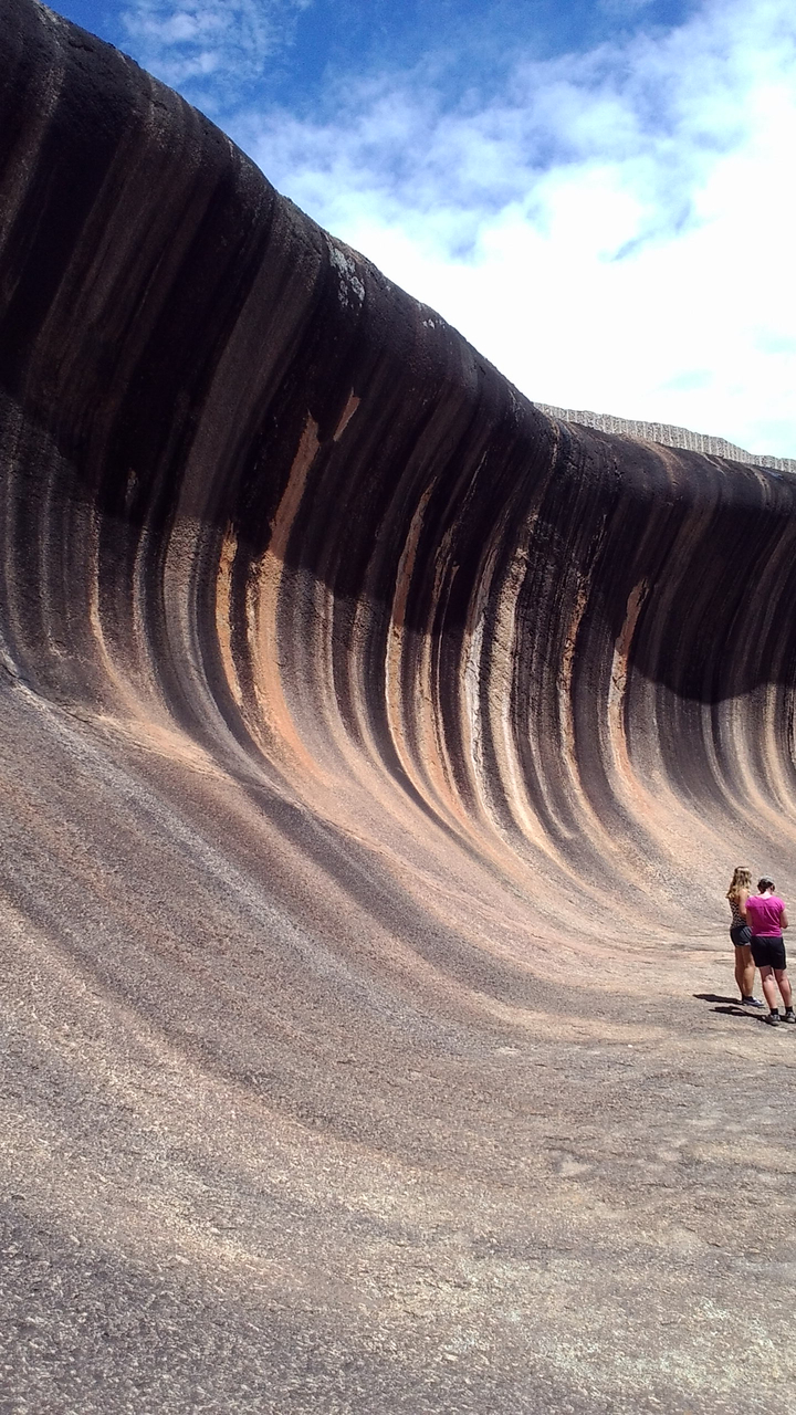 Deux personnes regardant une grande formation rocheuse naturelle en forme de vague.