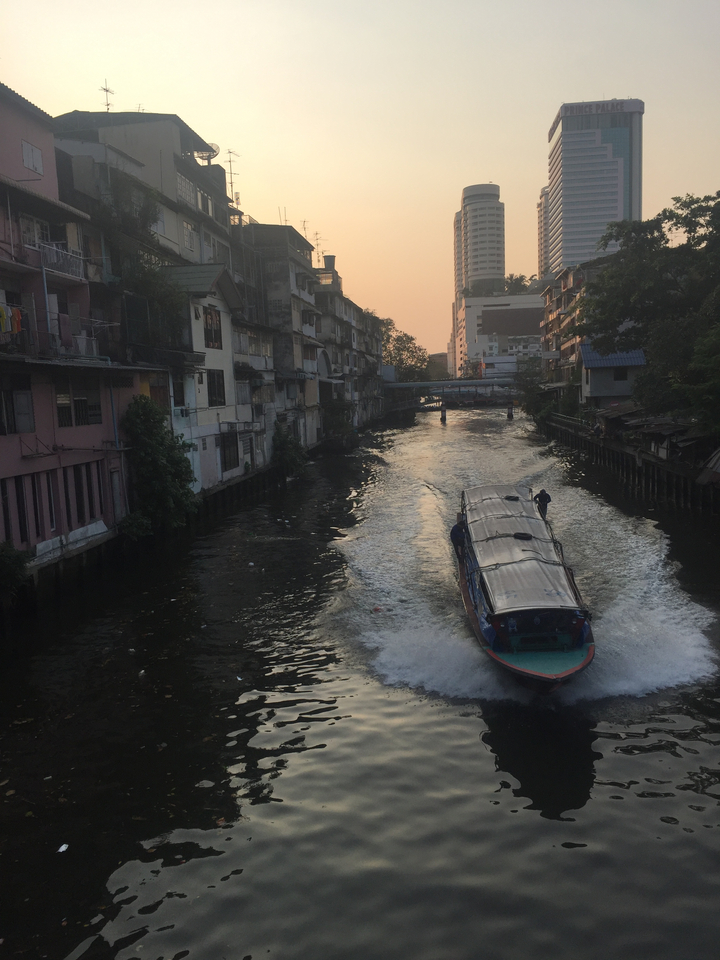 Boat navigating a narrow city canal during sunset.