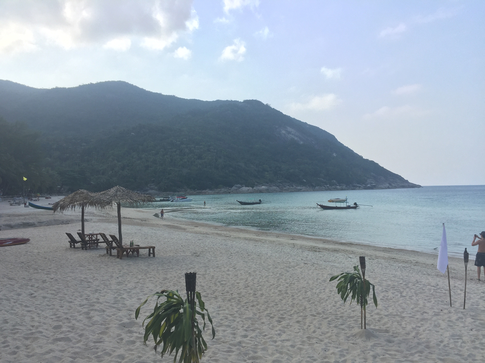 Beach scene with a few chairs under a straw umbrella.