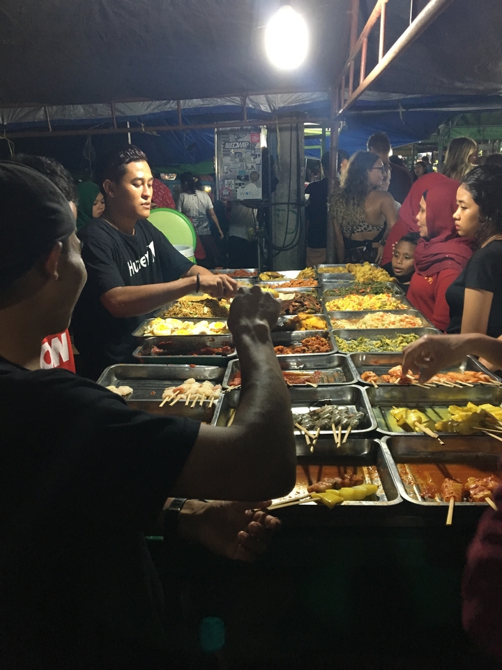 Un stand de nourriture très fréquenté où les gens choisissent divers plats sur des plateaux métalliques.