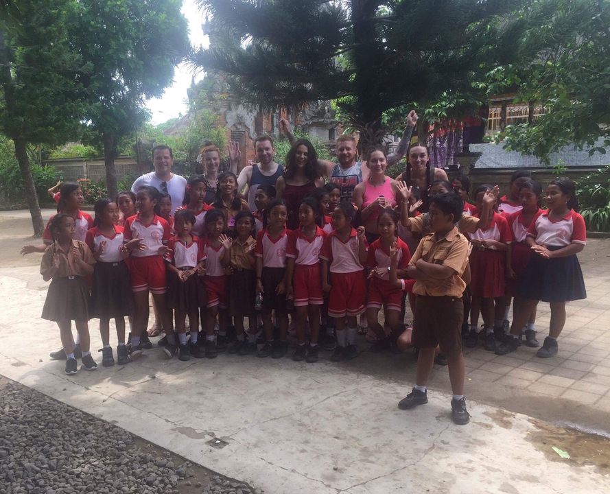 Un grand groupe d'enfants en uniforme scolaire posant avec des touristes devant un bâtiment.