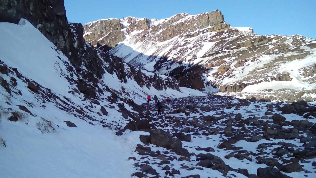 A snowy rocky path leading to majestic mountains under a clear sky.