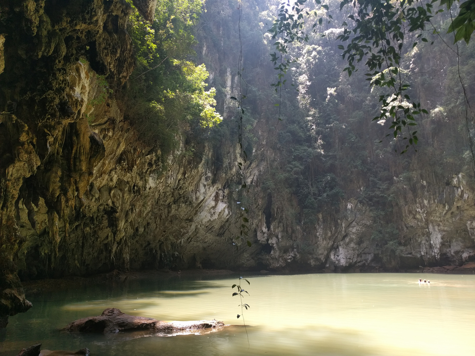 Cave with a serene pool of water and sunlight filtering in.