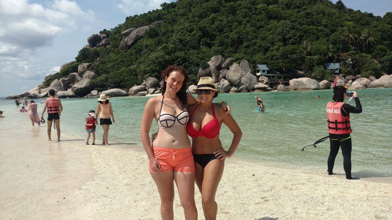 Two women posing on a beach with a lush backdrop.