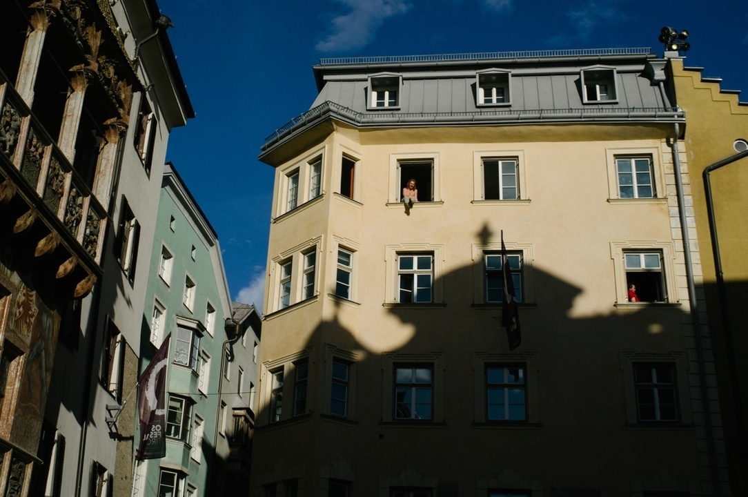 Rue avec des bâtiments architecturaux projetant des ombres sous un ciel clair.