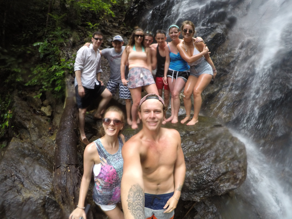 Group of people posing under a waterfall.