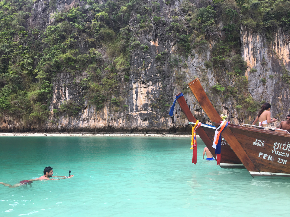 Person swimming in clear turquoise water with a traditional boat nearby.